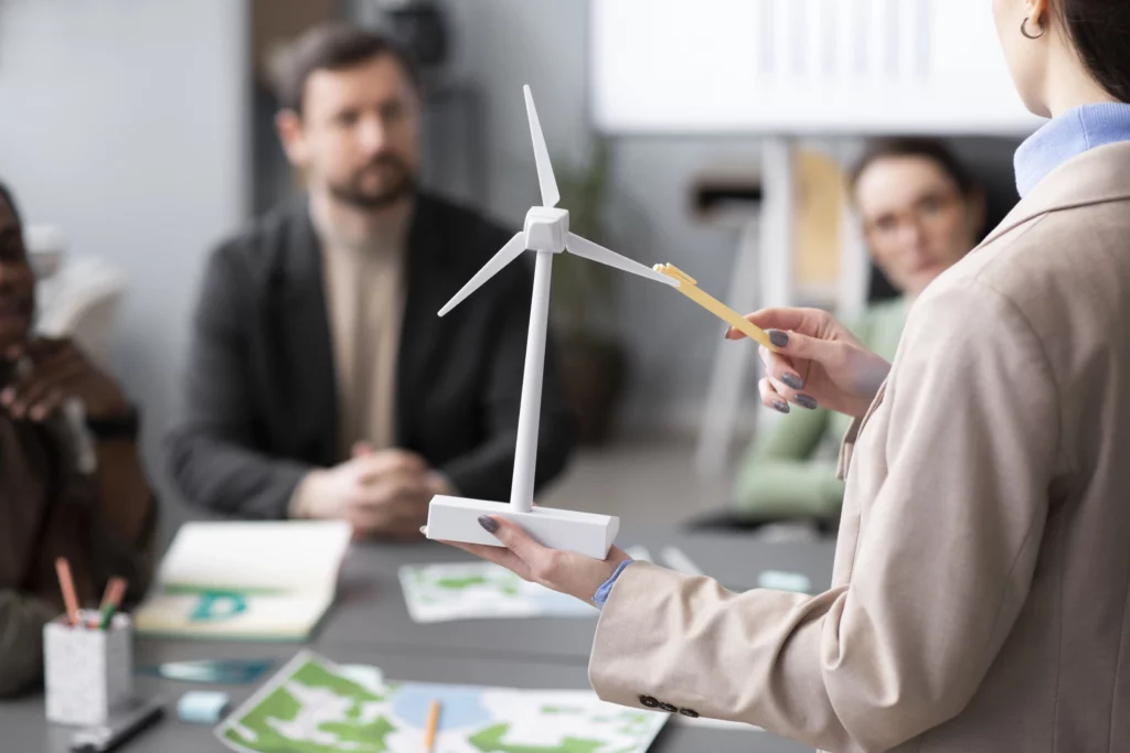 Picture of a lady showing with a pen a wind turbine miniature