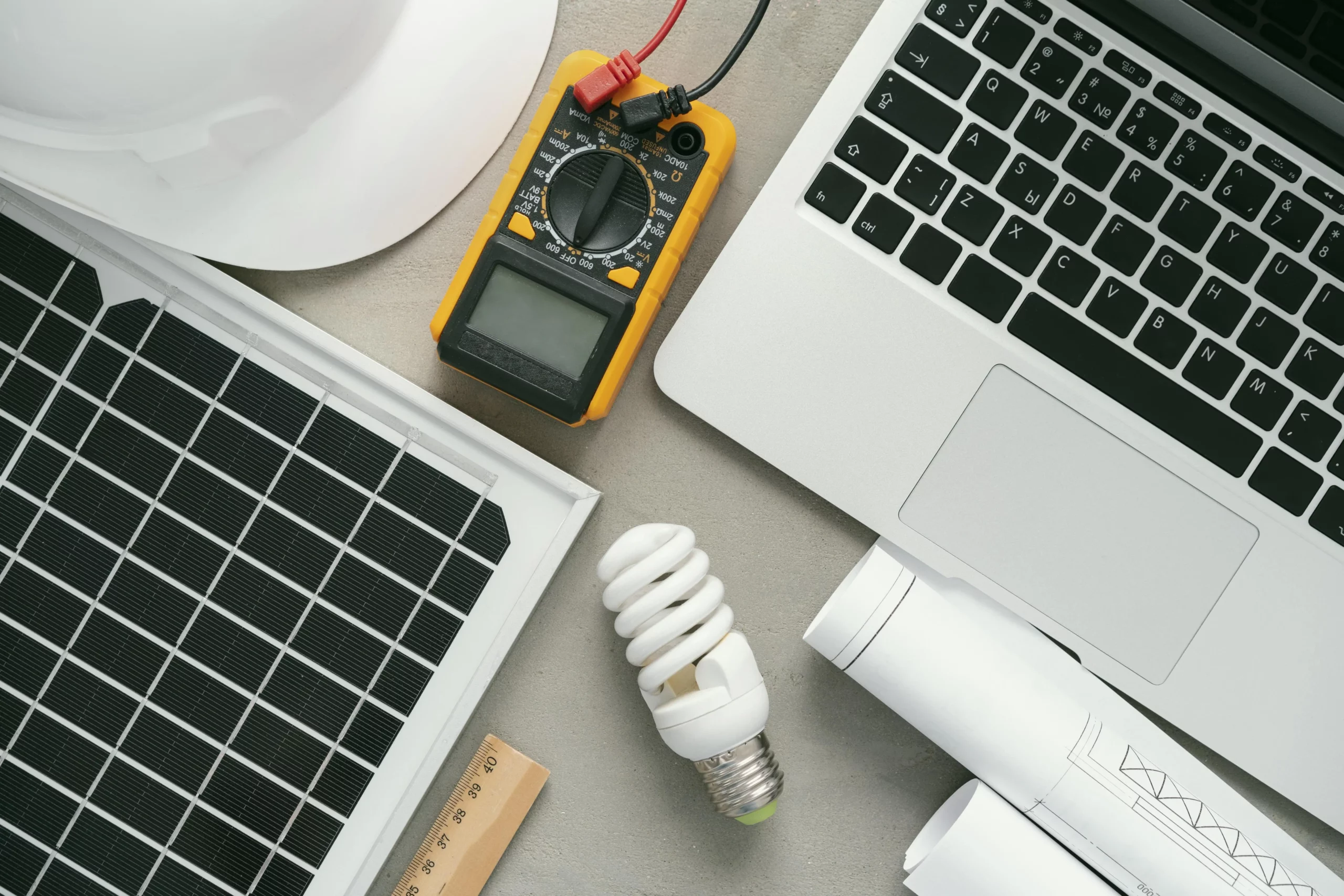 Picture with a lot of technical objects: computer, solar panel, lamp, meter, ruler, plans