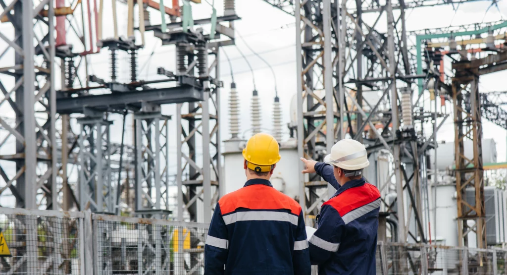 Two men wearing helmets looking at a transformer